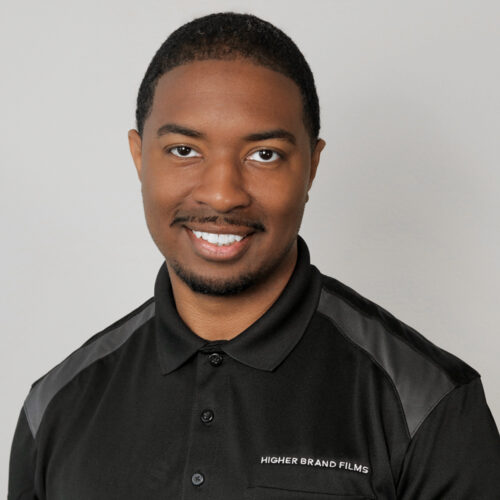 Brandon Hadnot, owner of Higher Brand Films - a multimedia production company, wearing a black and gray polo, smiling.